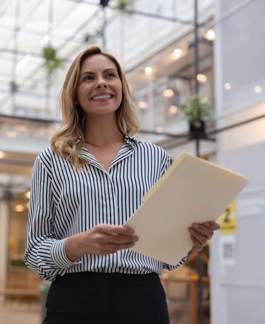 Smiling woman holding a folder in a bright office space.