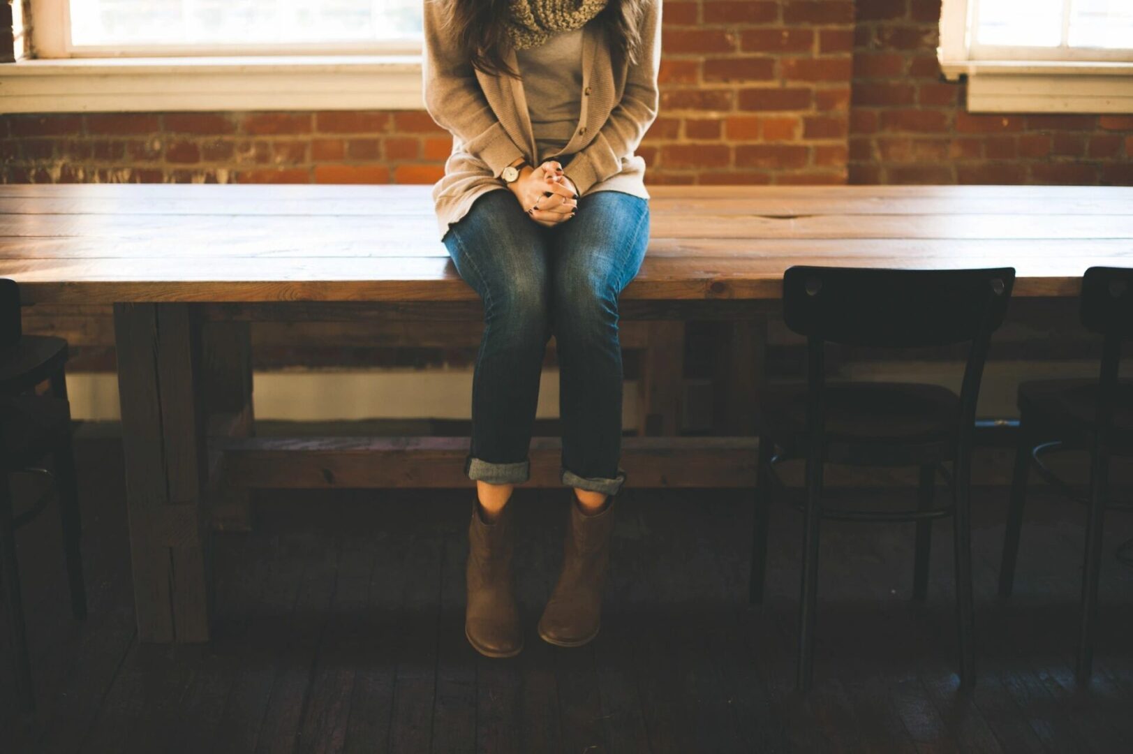 A woman sitting on a wooden table with a brick wall background.