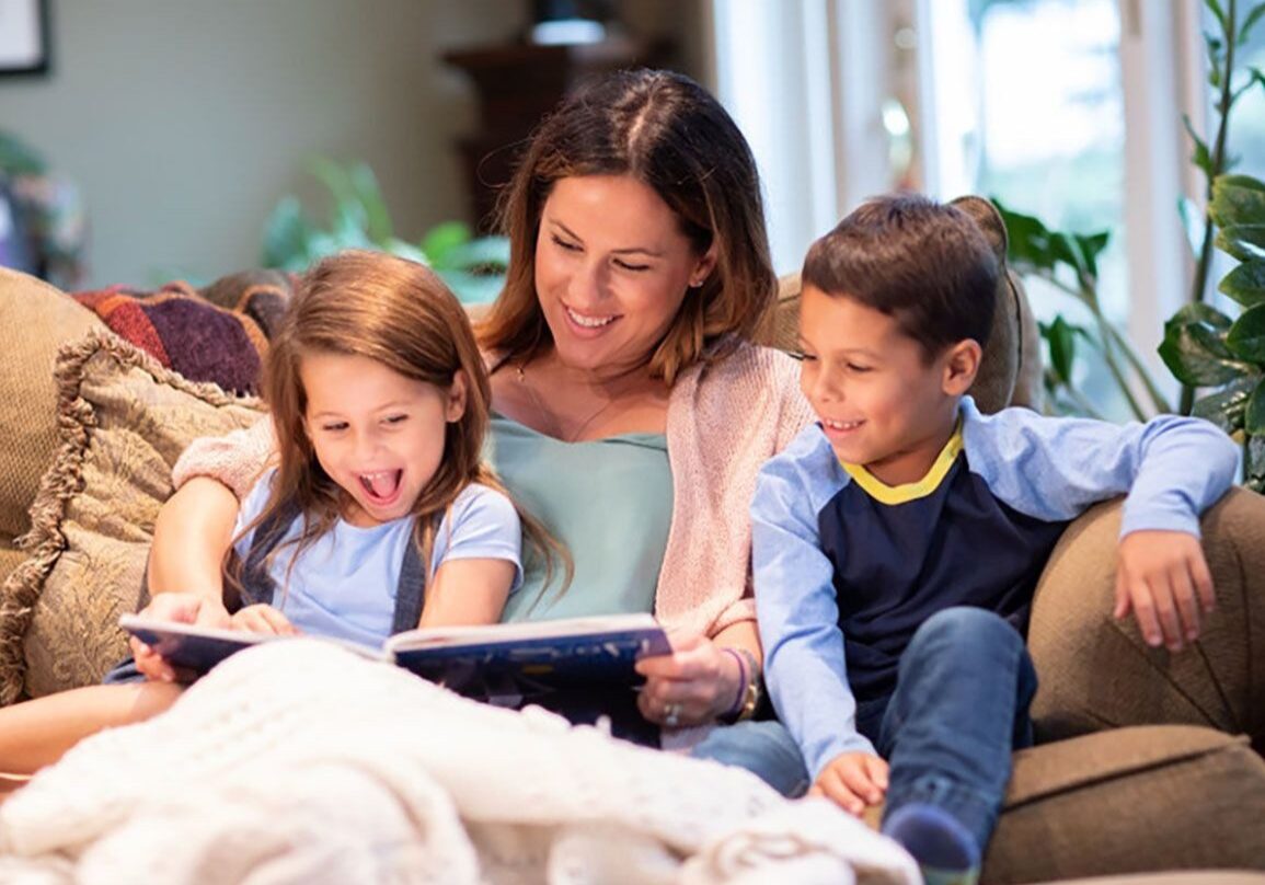 Mother reading a book with her two children on a cozy couch.